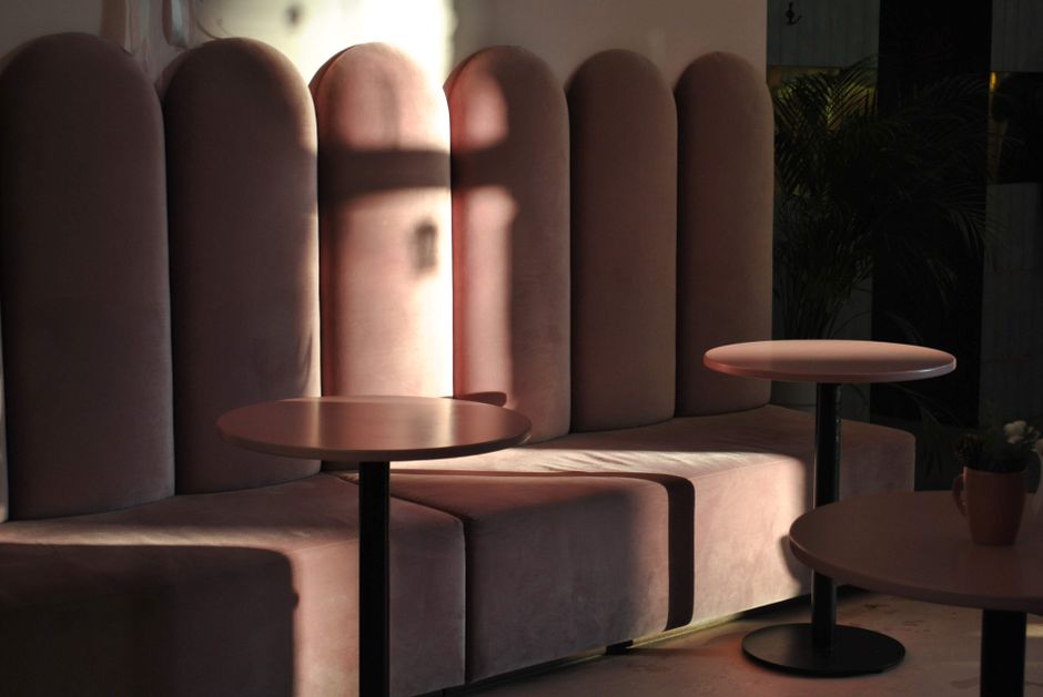 Inside a modern boutique cafe, there are multiple light wooden tables with beige table runners, each adorned with small white vases containing dried floral arrangements. Bright green upholstered chair